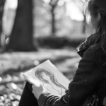 Grayscale image of a person drawing in the woods